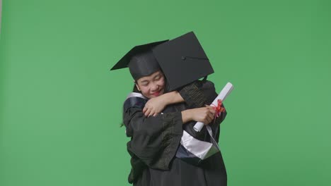 asian woman students graduate in caps and gowns with diplomas smiling and hugging each other on the green screen background in the studio