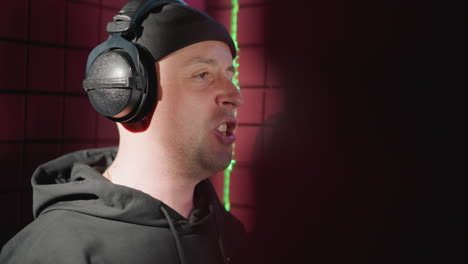 close-up of a man dressed in black, passionately singing into a microphone in a soundproofed recording room. the singer is wearing headphones and making expressive hand movements