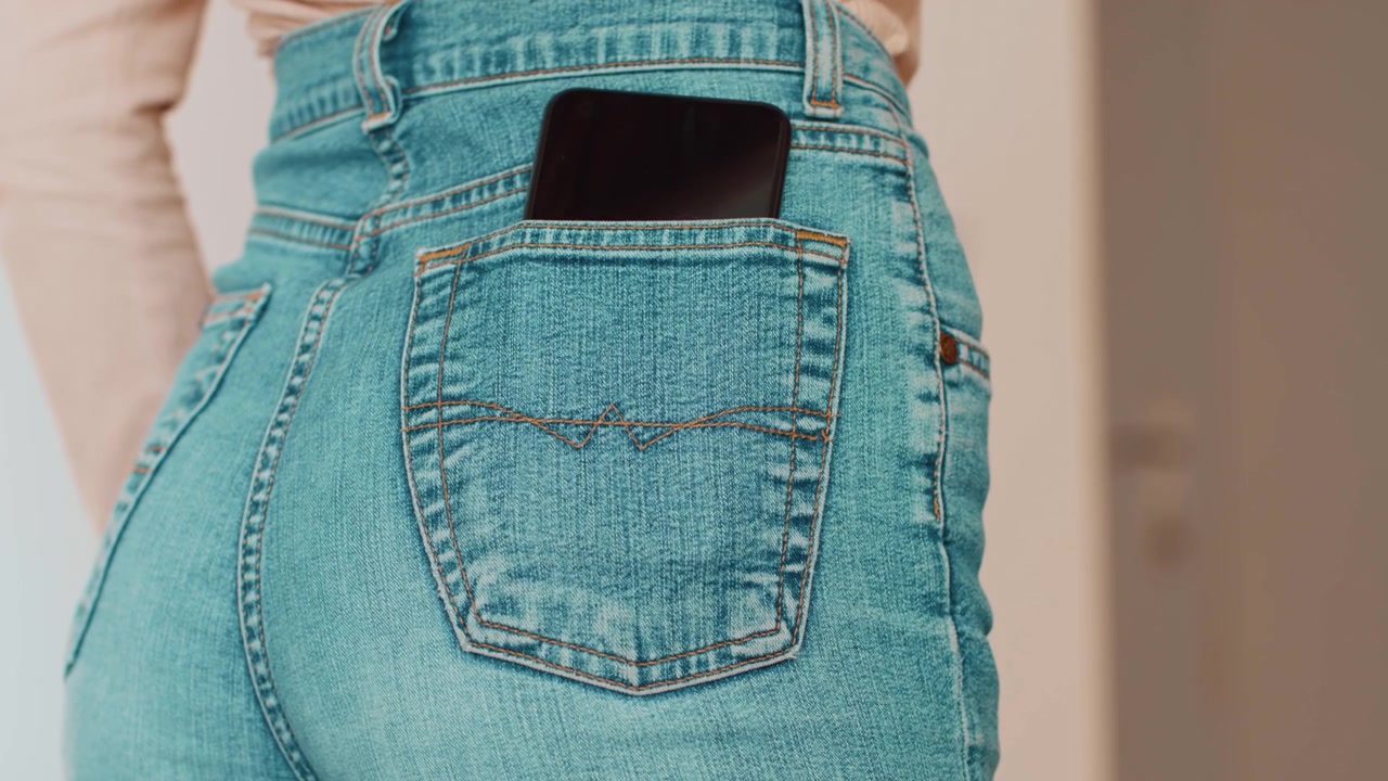 Woman Placing Smartphone into Back Pocket of Blue Jeans