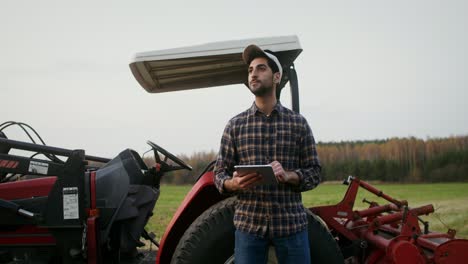 agricultor que utiliza una tableta cerca del tractor en el campo