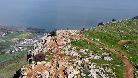 aerial forward shot of few people on a mud trail at the arbel cliff, galilee sea with sun rays in the background