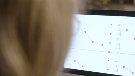 rear view of woman employee observing stadistics and graphics on computer monitor sitting at desk in the office 2