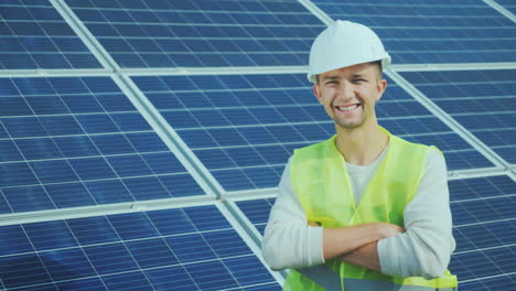 Retrato-De-Un-Trabajador-En-Overol-Y-Un-Casco-En-El-Fondo-De-Paneles-Solares-Sonrisas-Mira-A-Th