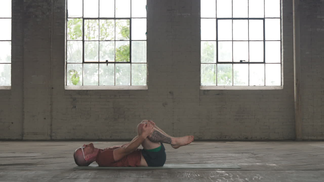 Timelapse footage of a man in an industrial warehouse setting doing a yoga flow.