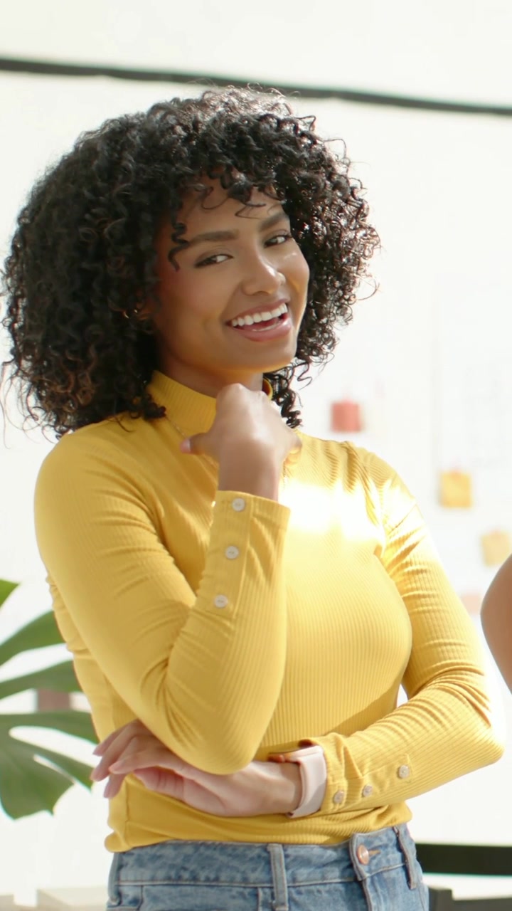 Vídeo vertical: Mulher sorrindo, tocando o queixo no estúdio após elogios, com blusa amarela e smartwatch