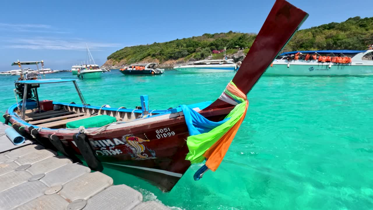 Wooden long-tail boat moored at floating dock, turquoise sea, bright daylight, tropical island background
