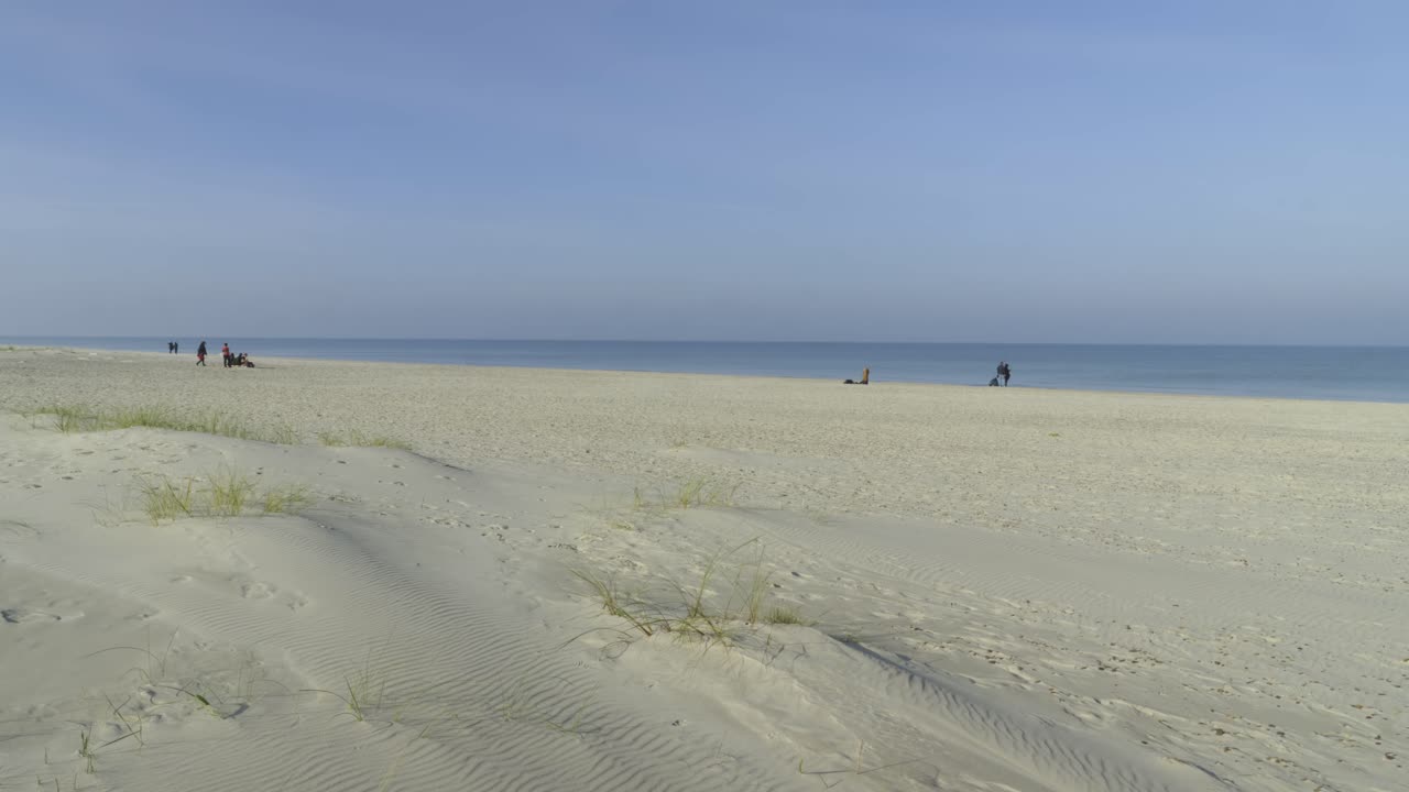 A large sandy beach by the Baltic Sea with a few people relaxing