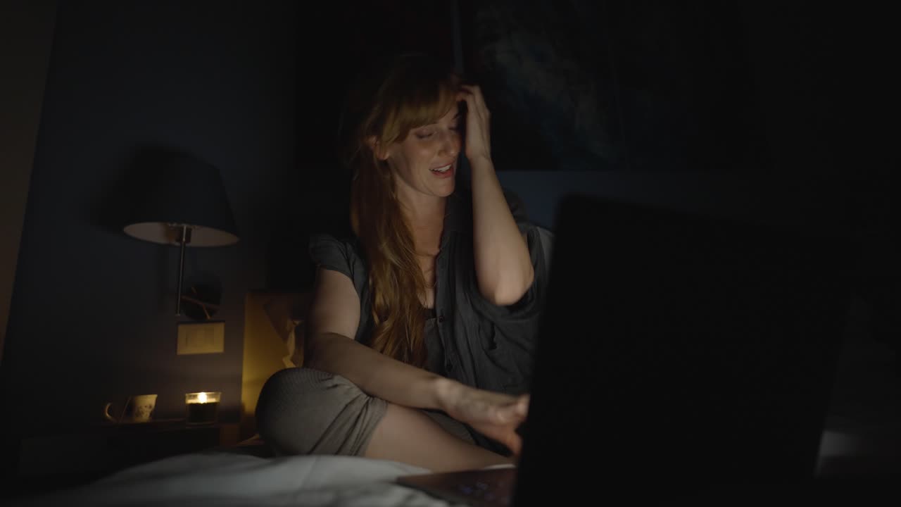 Woman sitting in her bed working late at night on her laptop computer