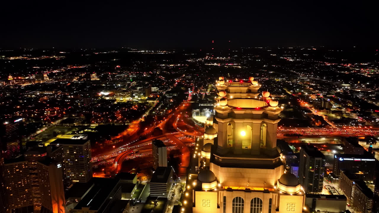 밤에 애틀랜타 시의 91 피치 트리 타워의 마천루 첨탑의 조명을 보여주는 공중  ⁇ 도 촬영 - 배경에는 애틀랜타의 조명된 도시 풍경과 함께 영화적인 도른 촬영