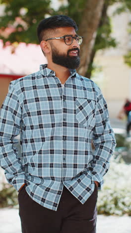 Happy-smiling-Indian-young-man-tourist-walking-in-urban-city-street-outdoors-in-summer-daytime