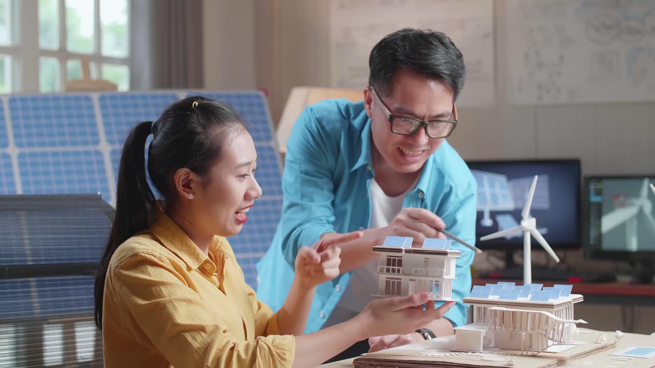 아시아인 남녀가 태양광 패널로 작은 집을 짓는 데 서로 도움을 주고 있습니다.