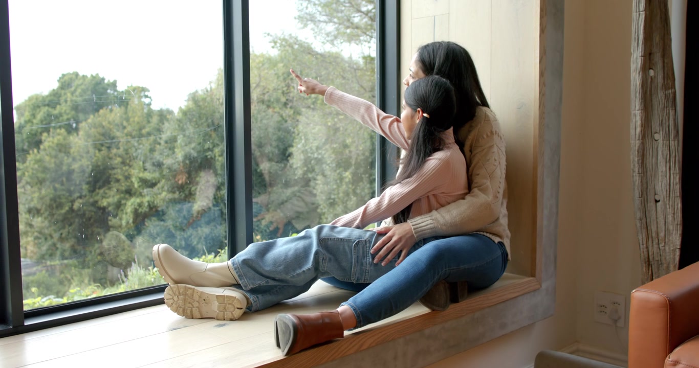 Madre che guida un bambino indiano sul davanzale della finestra, indicando le cime degli alberi, con un movimento avvistato all'esterno; spazio per il testo.
