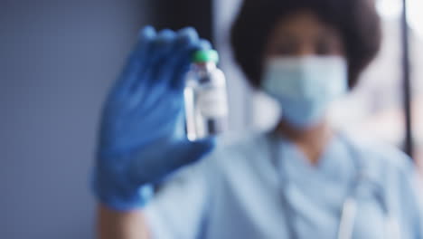 Mixed-race-female-doctor-wearing-face-mask-showing-medicine-to-the-camera