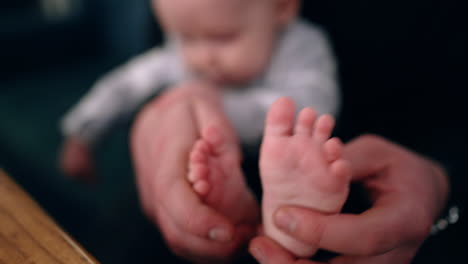 dad's hands hold the tiny feet of his baby. father tickles and claps son's feet. close up. blurred backdrop.