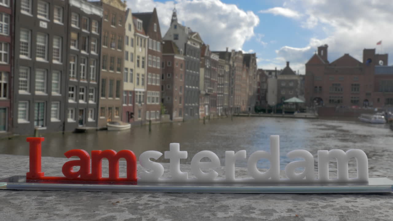 View of small plastic figure of Iamsterdam letters sculpture on the bridge against blurred cityscape Amsterdam Netherlands