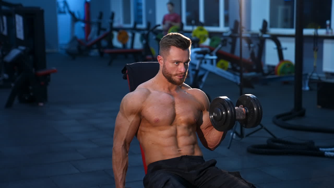 Young bodybuilder holding dumbbell. Muscular man training with dumbbell in the gym