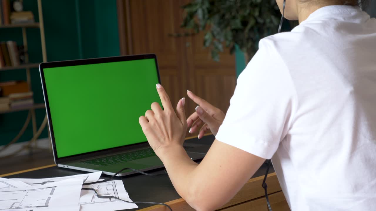 sobre el hombro de una mujer de negocios que trabaja en el interior de la oficina en la pc en el escritorio, mirando la pantalla verde. persona de la oficina usando una computadora portátil con pantalla verde portátil, sentada en una mesa de madera