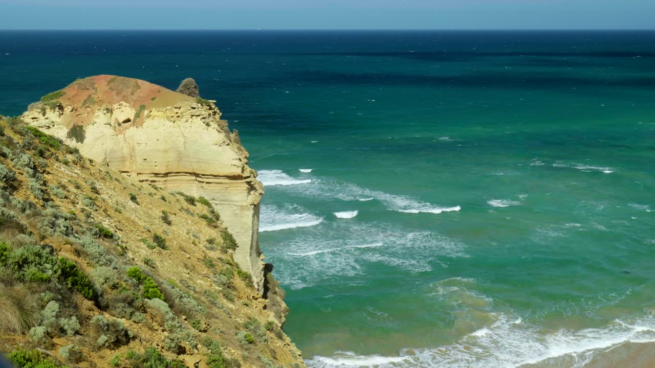 Waves breaking powerfully against rocks below a rugged cliff edge, showcasing the dynamic interaction between the sea and the coastline.