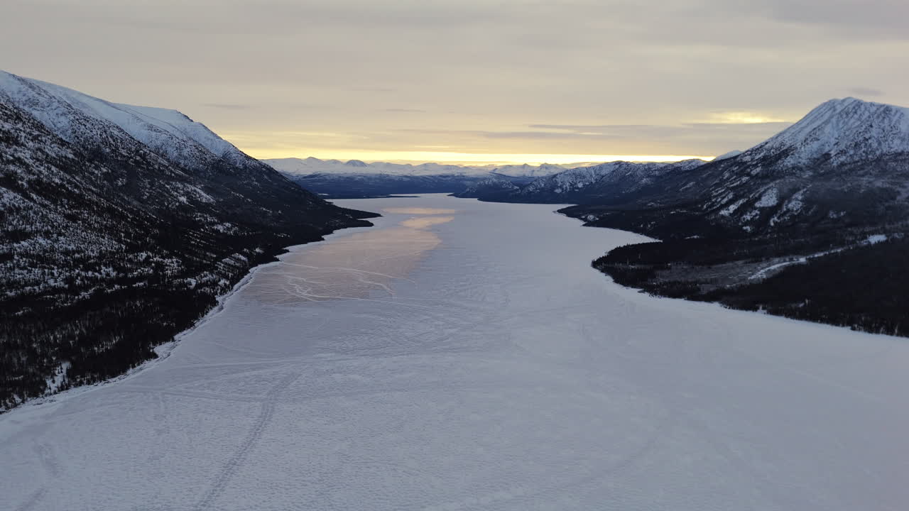 The Icy Surface of Kusawa Lake on the Takhini River at Sunset, Set Against the Winter Backdrop of Yukon, Canada - Aerial Drone Shot