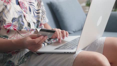 Close Up Of Hand Holding Credit Card And Using Laptop Computer Shopping Online In Living Room