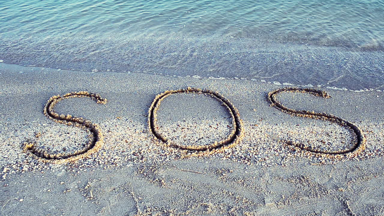 Indskriften SOS i sandet. Optagelse på stranden.