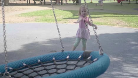 cámara lenta de una niña de 4 años vestida de rosa está jugando con un swinger en un patio de recreo durante un día soleado