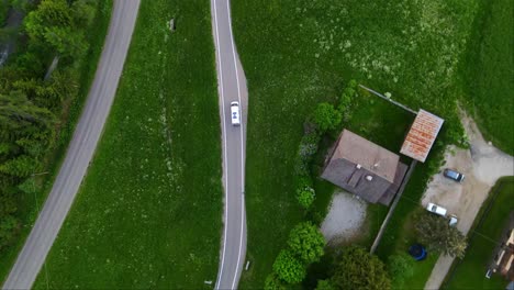 White-camper-van-driving-through-the-winding-mountain-road-around-the-alps---drone-top-view