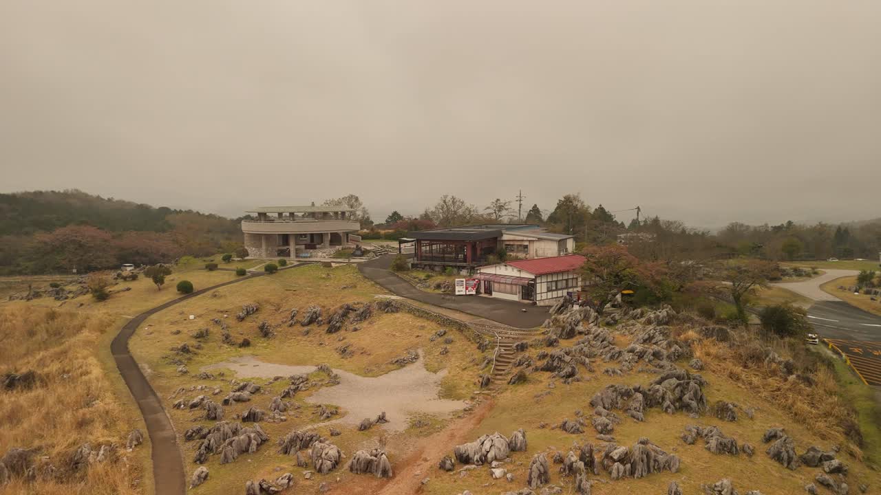 Aerial pan left across the Akiyoshidai visitor center in Japan. The unique karst landscape with its limestone rocks and dry autumn grass is covered in a moody, atmospheric fog.