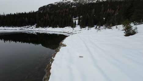 lago palu aerial fpv view following snowy woodland shoreline speeding across frozen valley lake