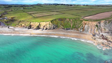 drone seascape of killfaracey beach waterford ireland with green fields sloping down to cliffs and the sea and emerald clear seas