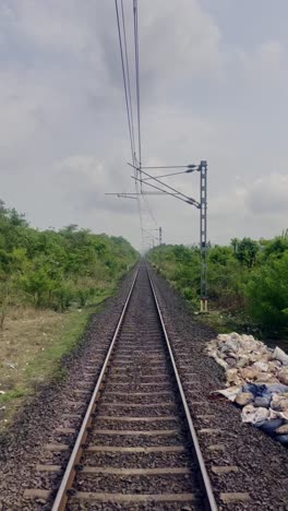 train tracks stretch forward, flanked by gentle, grassy hills on both sides. the sky above is cloudy maharashtra india 4k