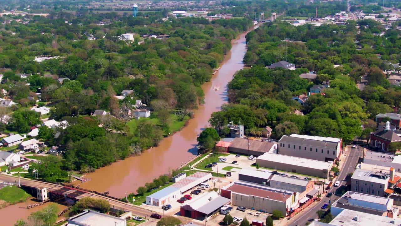 A drone tracks Bayou Teche through downtown New Iberia, Louisiana. The shot shows the bridge, Sliman Theatre, civic center, marina, and library, highlighting the cultural and waterfront district
