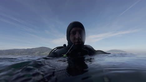 buzo en traje de buceo sin máscara mirando alrededor por encima del agua de la costa