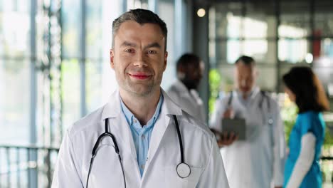 retrato de un médico masculino feliz con bata blanca mirando la cámara, sonriendo y de pie en la clínica