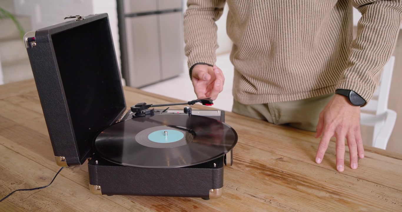 Handen pakken zwart vinyl op, plaatsen het op een draagbare platenspeler op tafel, laten de toonarm zakken om af te spelen.