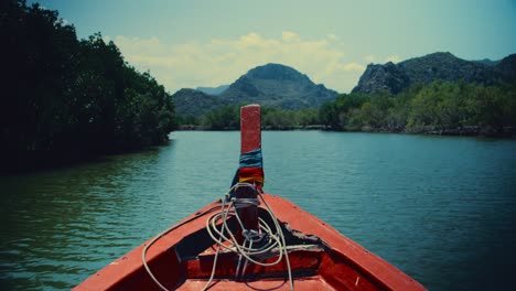 sitting in the front of a red long-tailed boat while sailing down a river in thailand