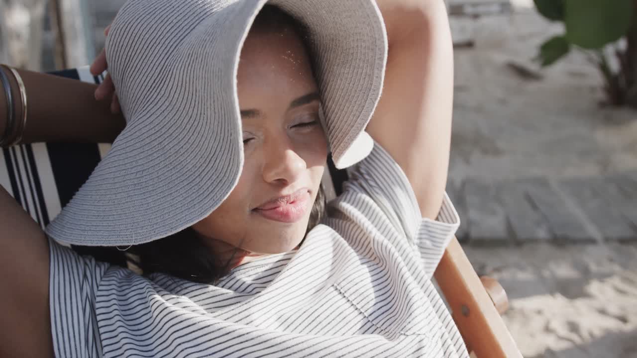 행복한 두 인종의 여성이 이 많은 해변에서 침대 의자에서 느린 동작으로 휴식을 취하고 있습니다.