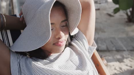 행복한 두 인종의 여성이 이 많은 해변에서 침대 의자에서 느린 동작으로 휴식을 취하고 있습니다.