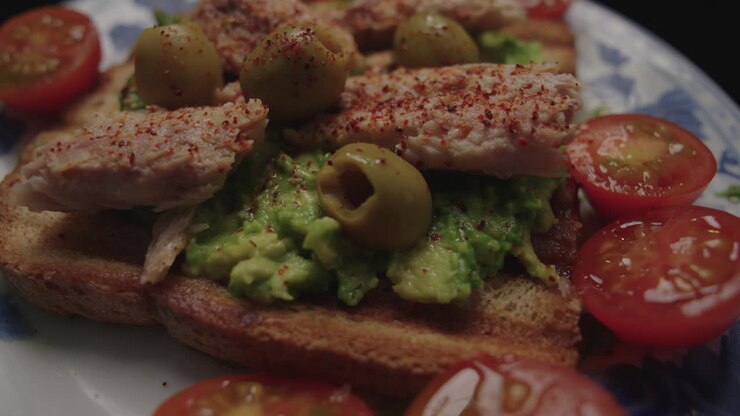 Primo piano di un toast all'avocado con tonno, olive verdi e pomodorini servito su un piatto