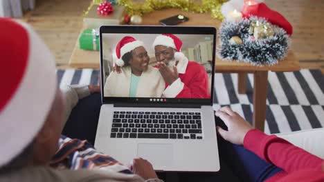 African-american-mother-and-daughter-using-laptop-for-christmas-video-call-with-couple-on-screen