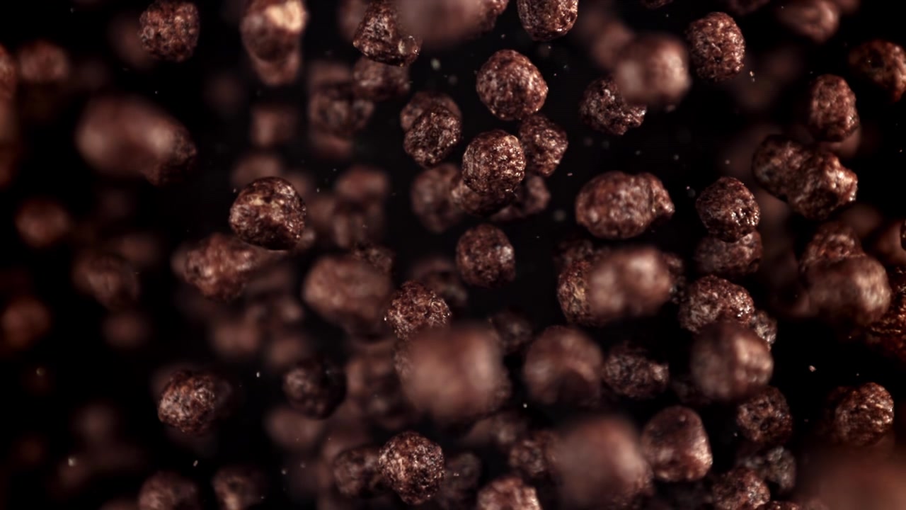 Palline di cereali al cioccolato che cadono al rallentatore su sfondo scuro.
