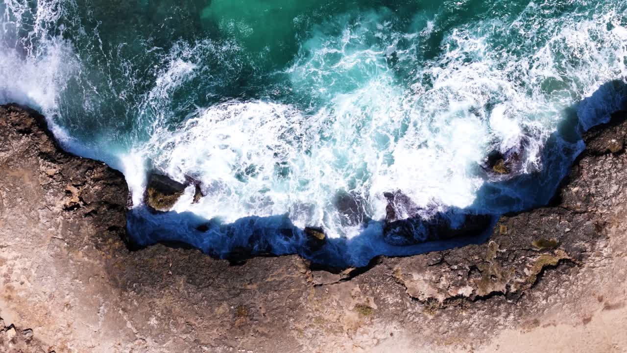 Onde oceaniche spumeggianti che si infrangono con forza sulla costa rocciosa, vista aerea dall'alto