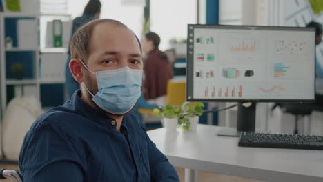employee with protection mask sitting on wheelchair in front of camera