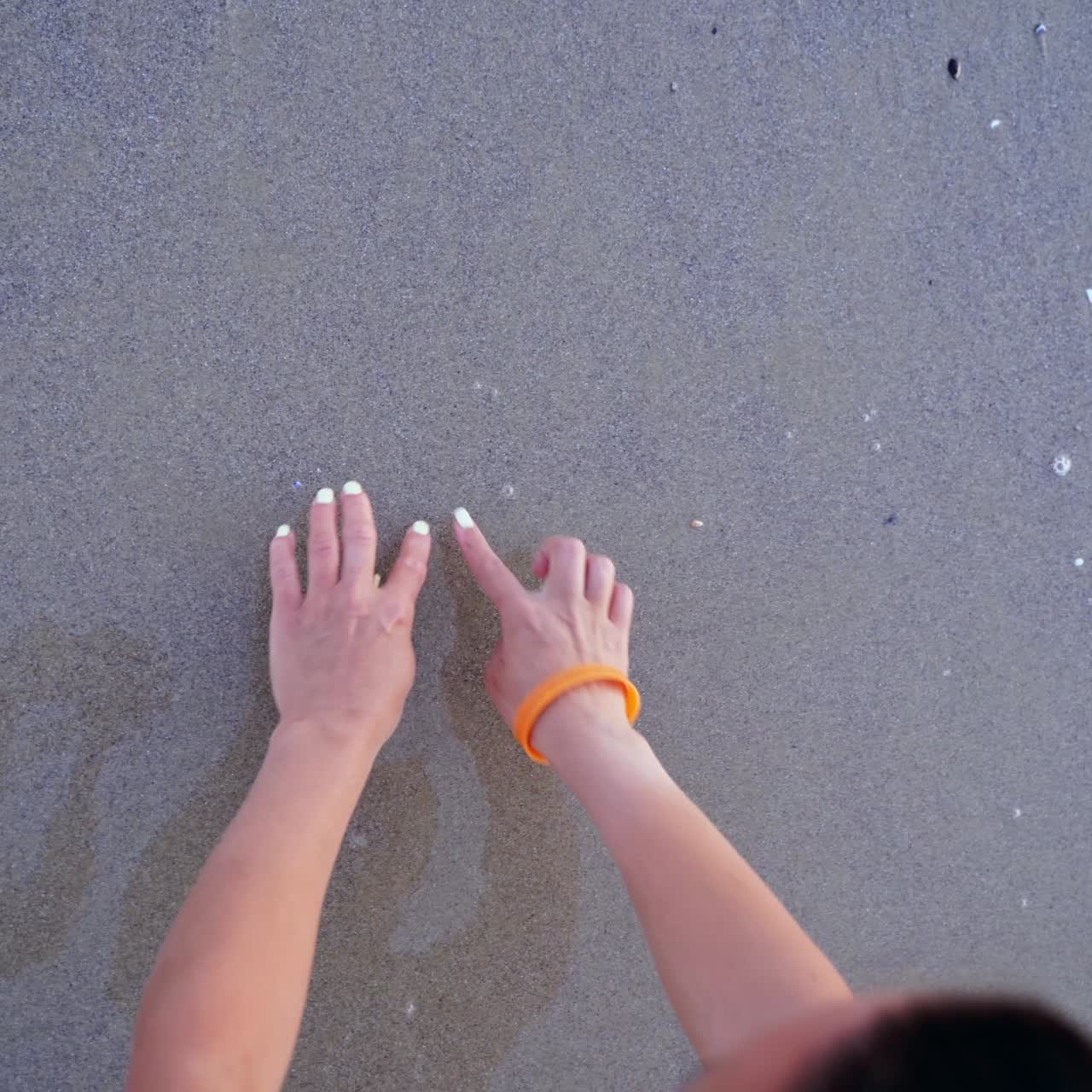 Woman draws heart on a wet sand. Female's hands writing the word sea on sand. Sea water washes away the drawing on a sandy beach.