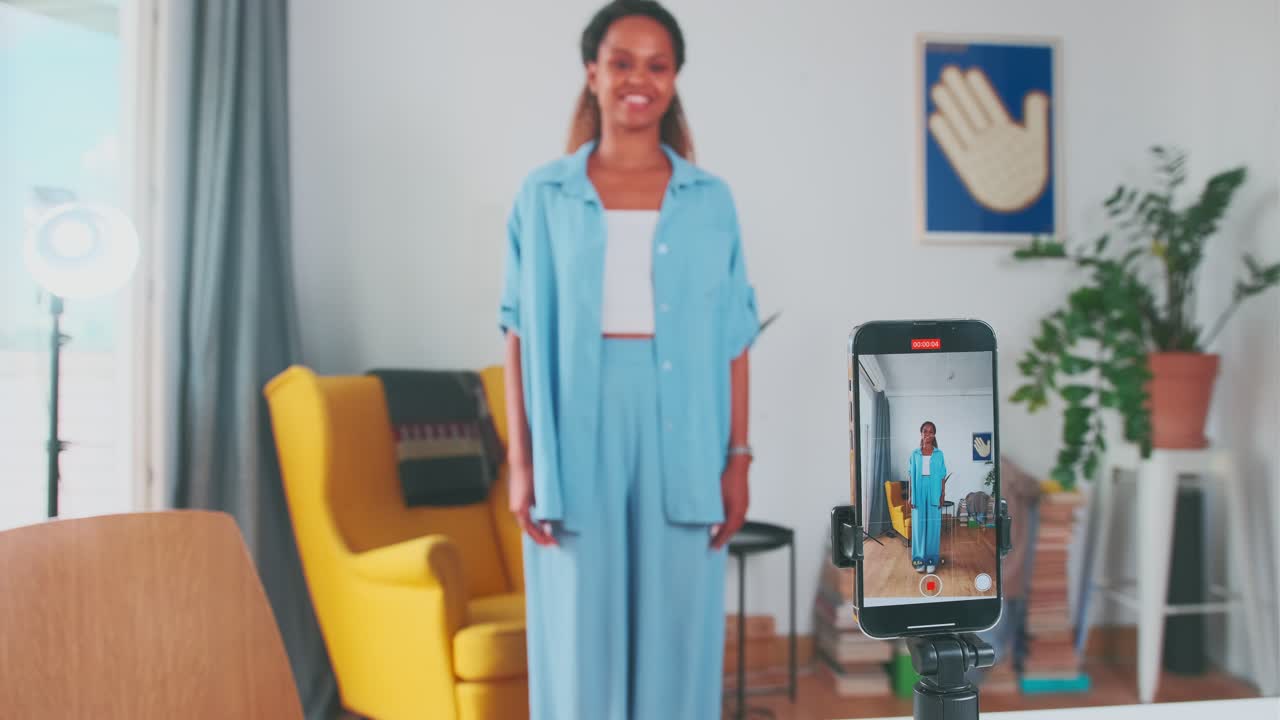Young cheerful african american woman records vertical video of dance on phone