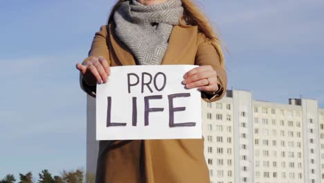 attraktive frau, die papier mit pro-life-wörtern mit stadtbild im hintergrund hält