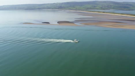 aerial static view of boat cruising on ocean in front of island on sunny day