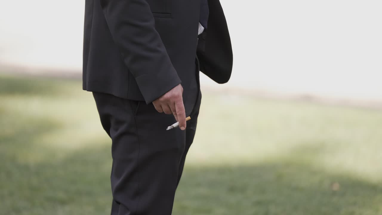 hombre en traje sosteniendo un cigarrillo al aire libre, destacando el tabaquismo y las preocupaciones de salud