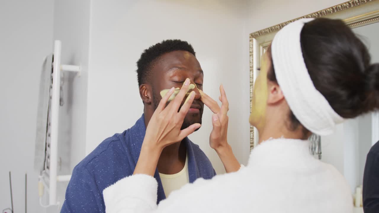 Happy diverse couple looking at each other and doing make up in bathroom