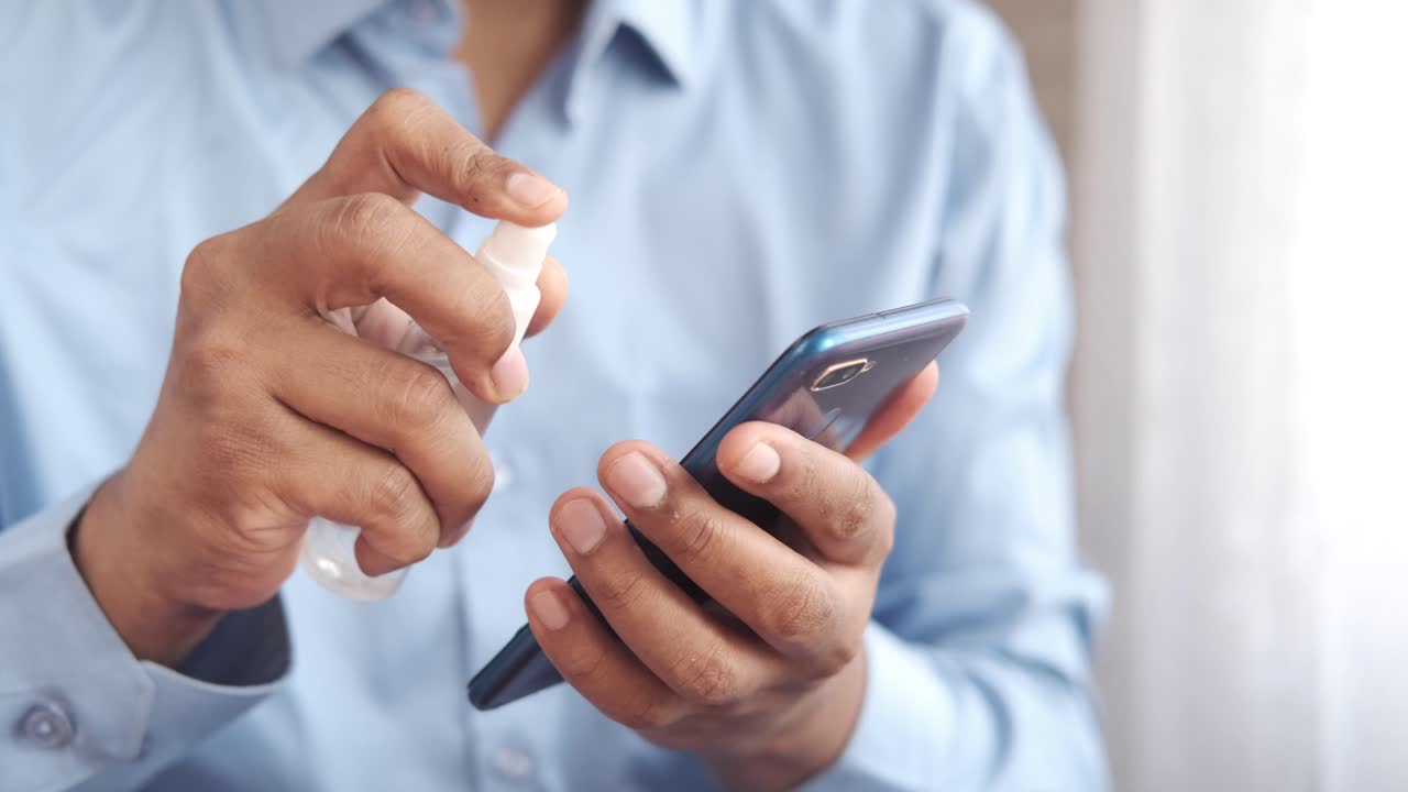 persona desinfectando un teléfono inteligente con desinfectante para manos
